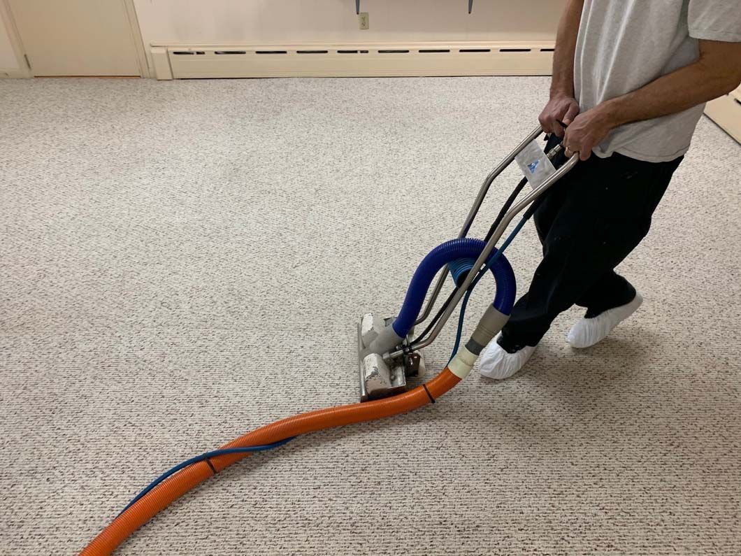 A person using a carpet cleaning machine on a light-colored carpet in a room.