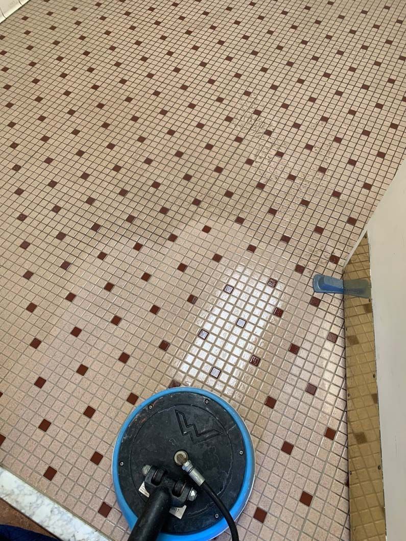 A floor cleaning machine works on a light-colored, patterned mosaic tile floor, creating a clean, shiny path.