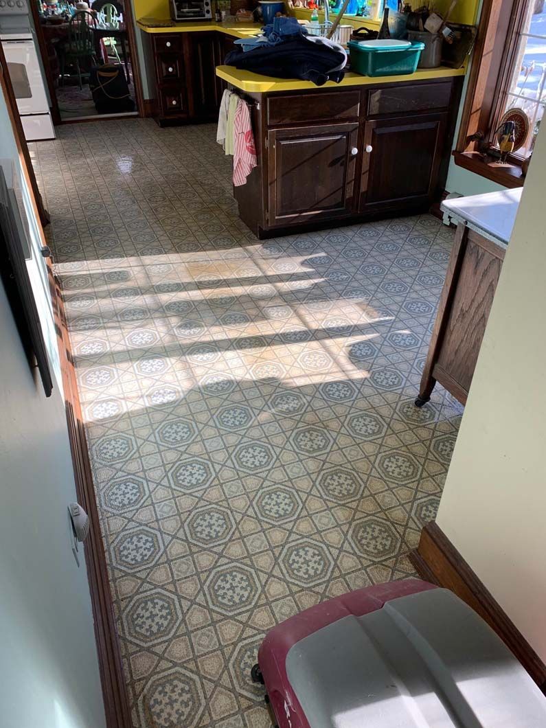 A kitchen view with patterned gray and white tiled floors, dark wood cabinets, a yellow counter, and a light-filled room.