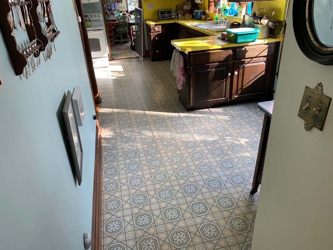 A hallway with patterned tile floors leads into a kitchen with dark wooden cabinets and yellow walls.
