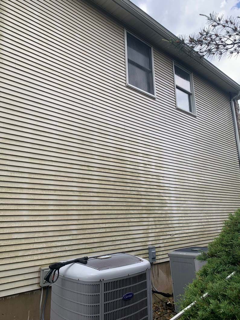 A cream-colored vinyl-sided house wall with visible dirt buildup near two outdoor air conditioning units.