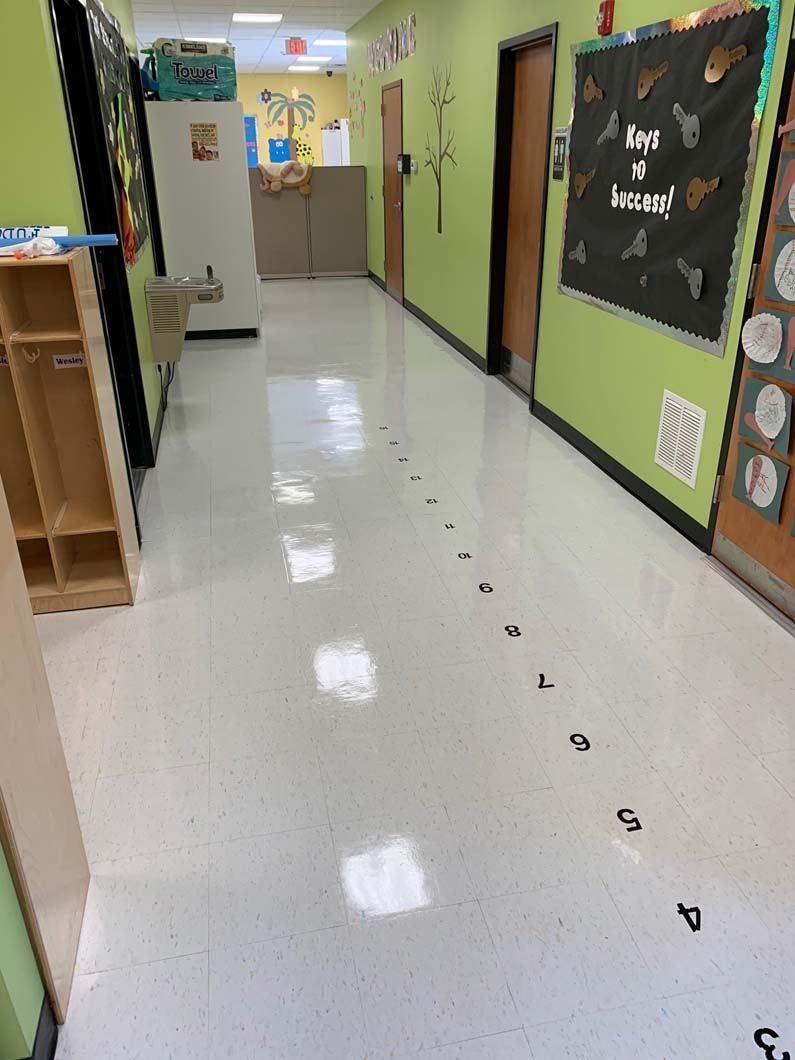 A brightly lit school hallway with lime green walls and a sequence of numbers from 3 to 10 marked on the floor tiles.