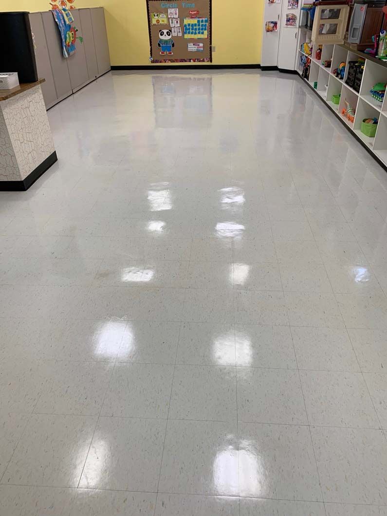A polished, light-colored floor in a classroom with cubbies, a bulletin board, and ceiling light reflections.