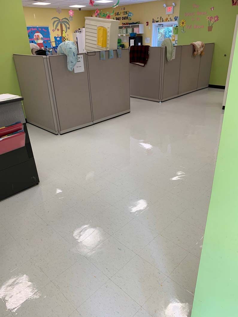 A daycare room with light green walls and white tiled floors marked by several light-colored, dusty footprints.
