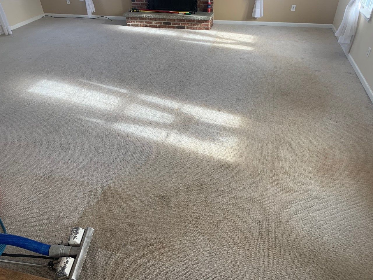 A vacuum cleaning wand on a beige, partially cleaned carpet in a room with a fireplace in the background.
