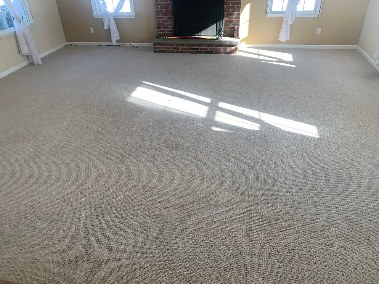 A carpeted room featuring a brick fireplace centered between two windows with white curtains.