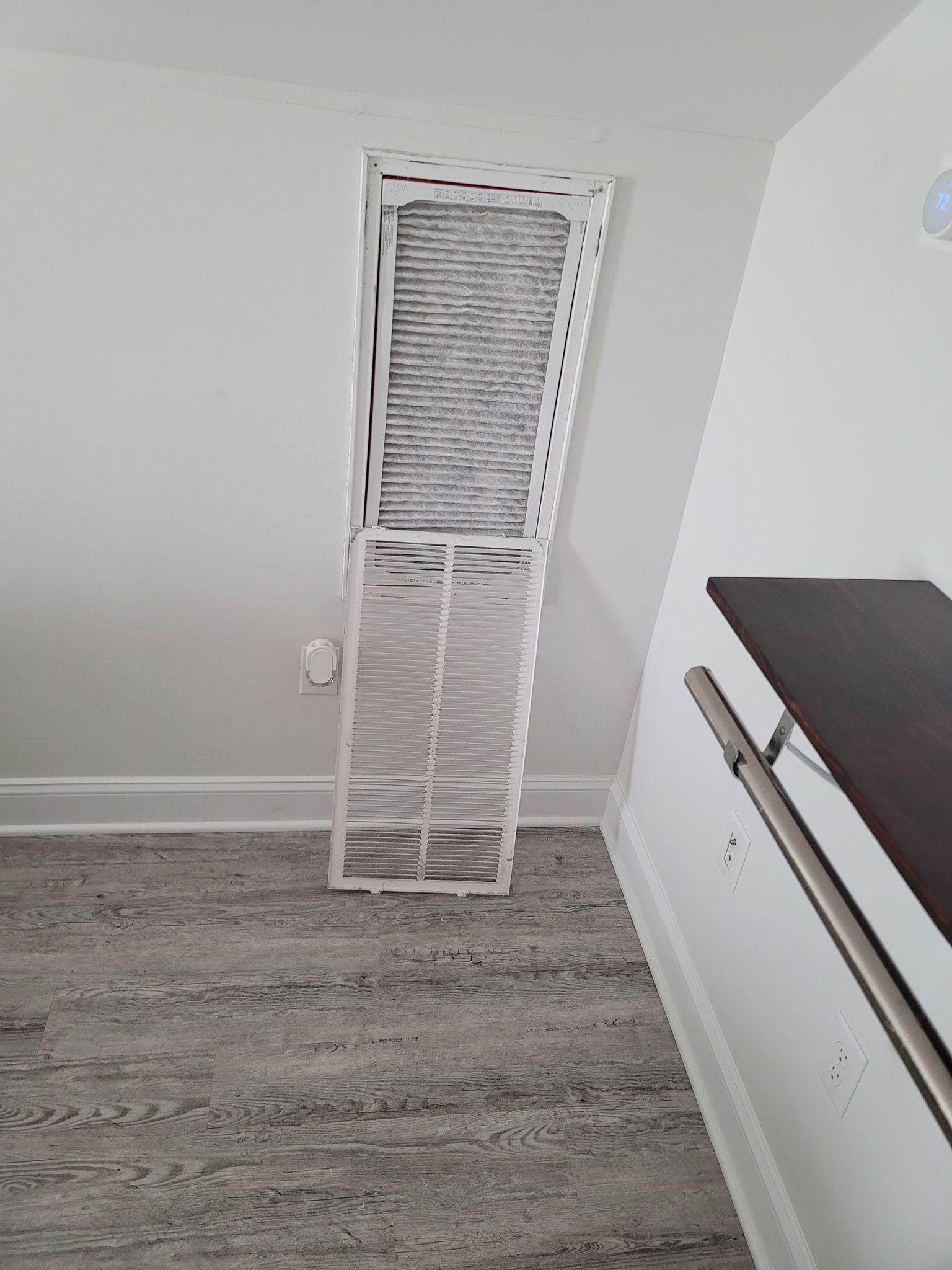 Open air vent with filter on a white wall, gray floor.