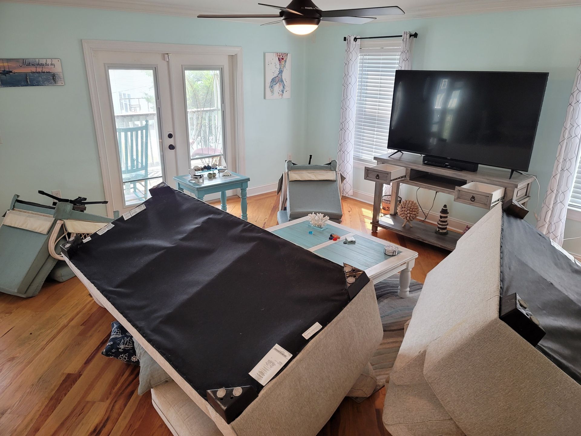 Living room with overturned furniture, TV, and balcony doors.