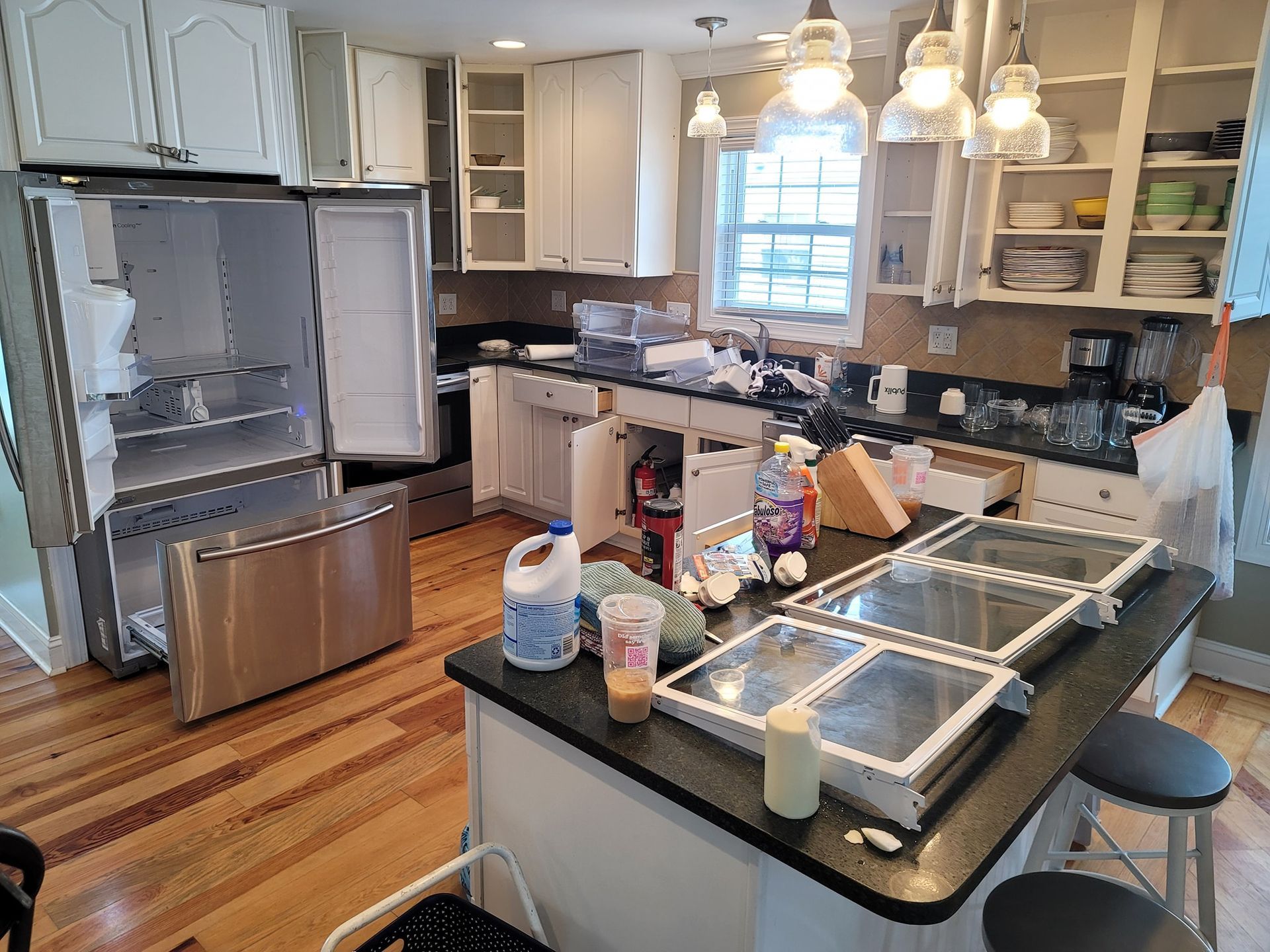 Kitchen in disarray; refrigerator open, cabinets empty. Counter with items on it.