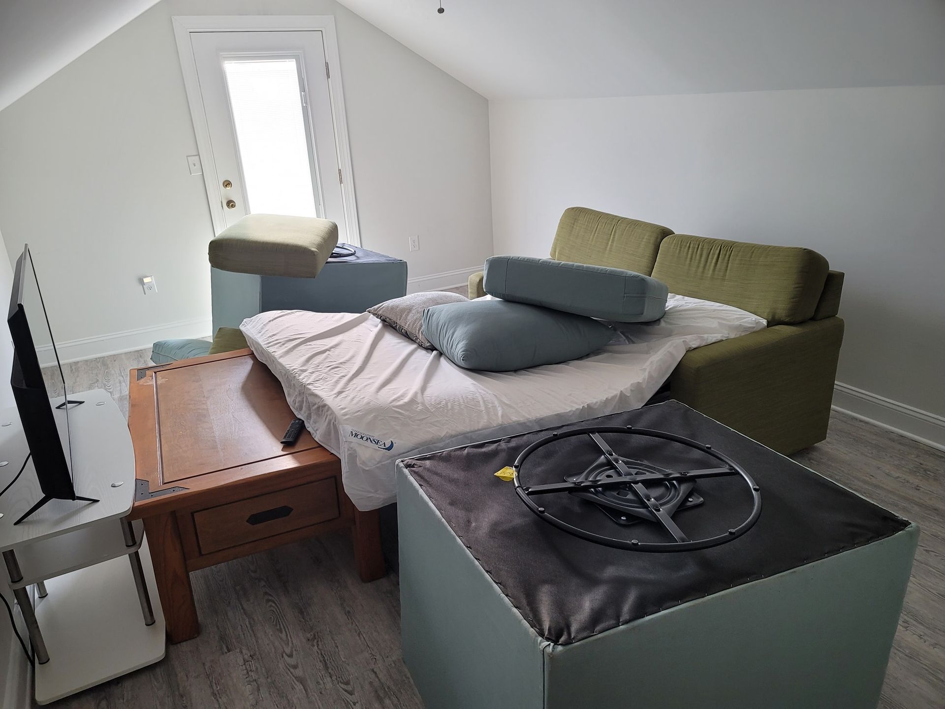 A room with furniture, including a bed, couch, and table; natural light from a window.