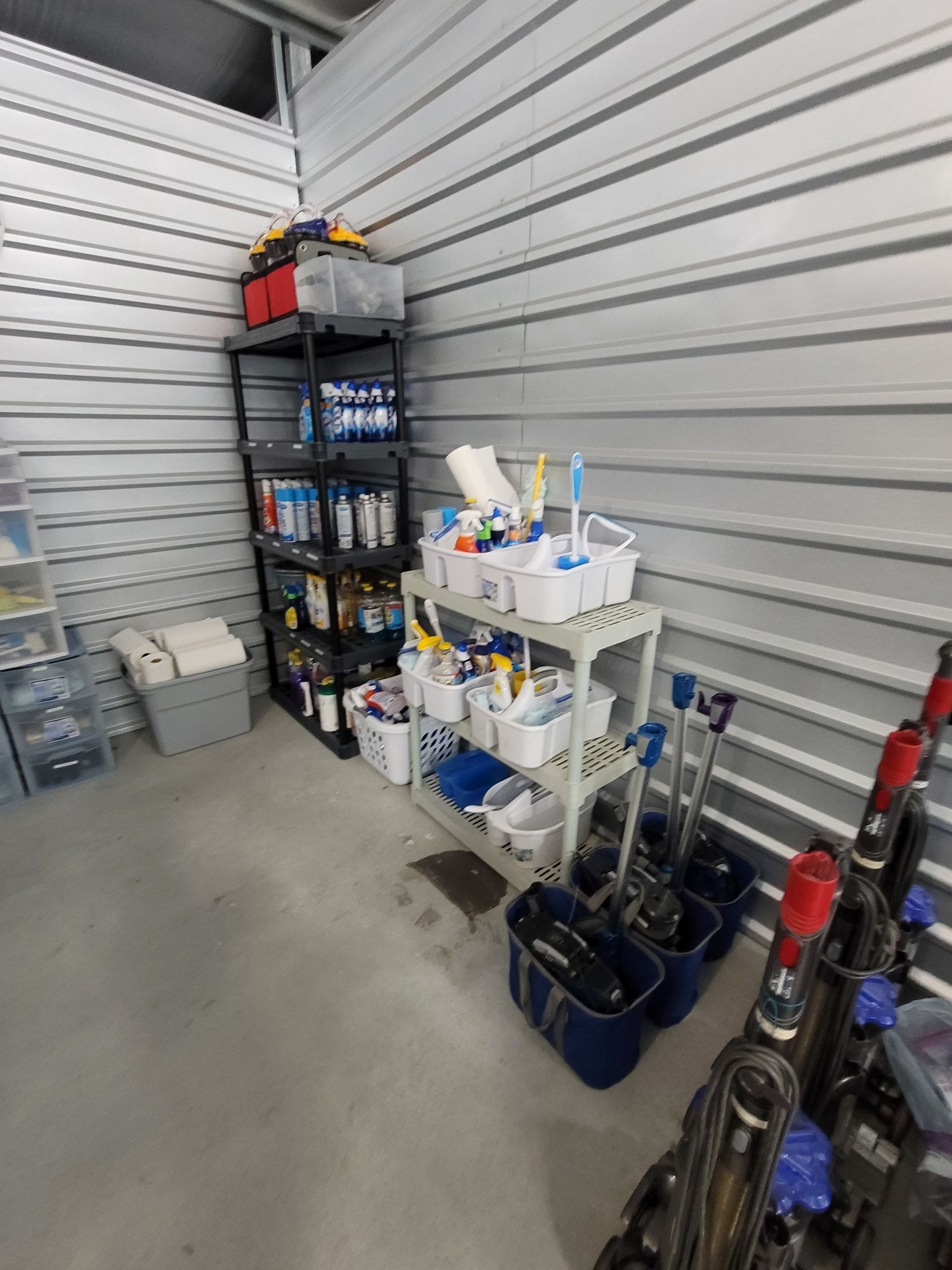 Storage unit with cleaning supplies on shelves, buckets, and mops; gray and white interior.