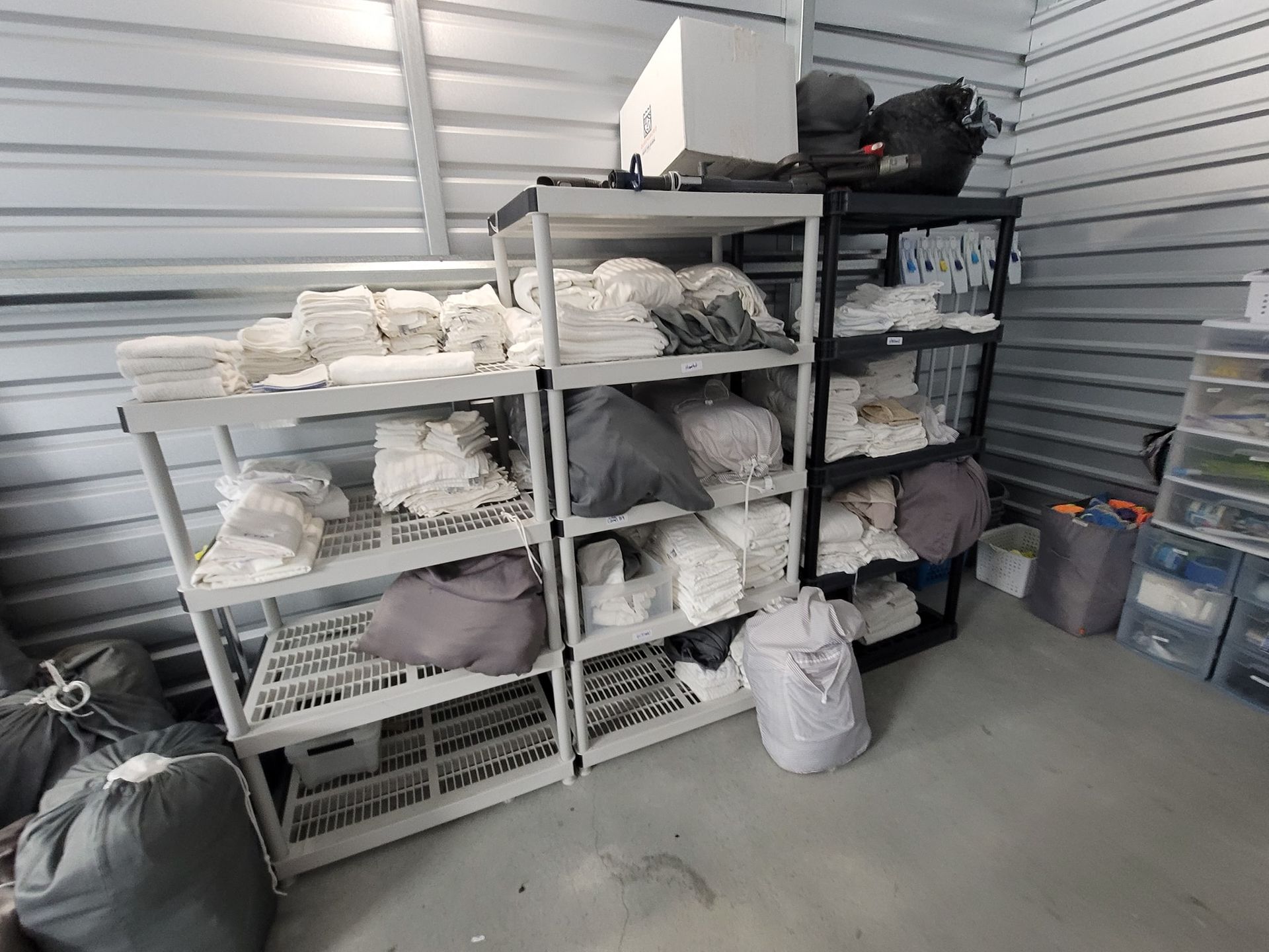 Shelves in a storage unit filled with bagged linens and items. Gray and black shelves against metal walls.