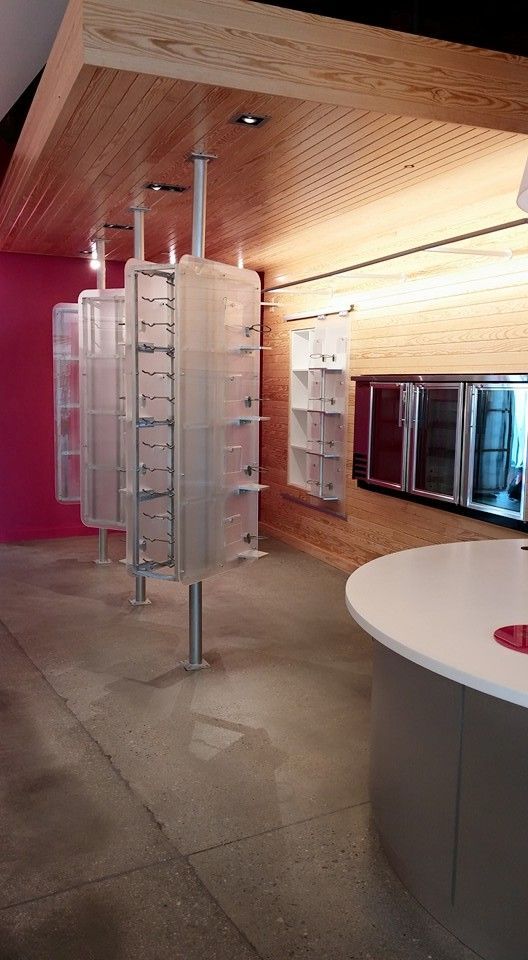 Modern retail display with cylindrical glass shelves, grey floors, pink wall, and wooden ceiling.