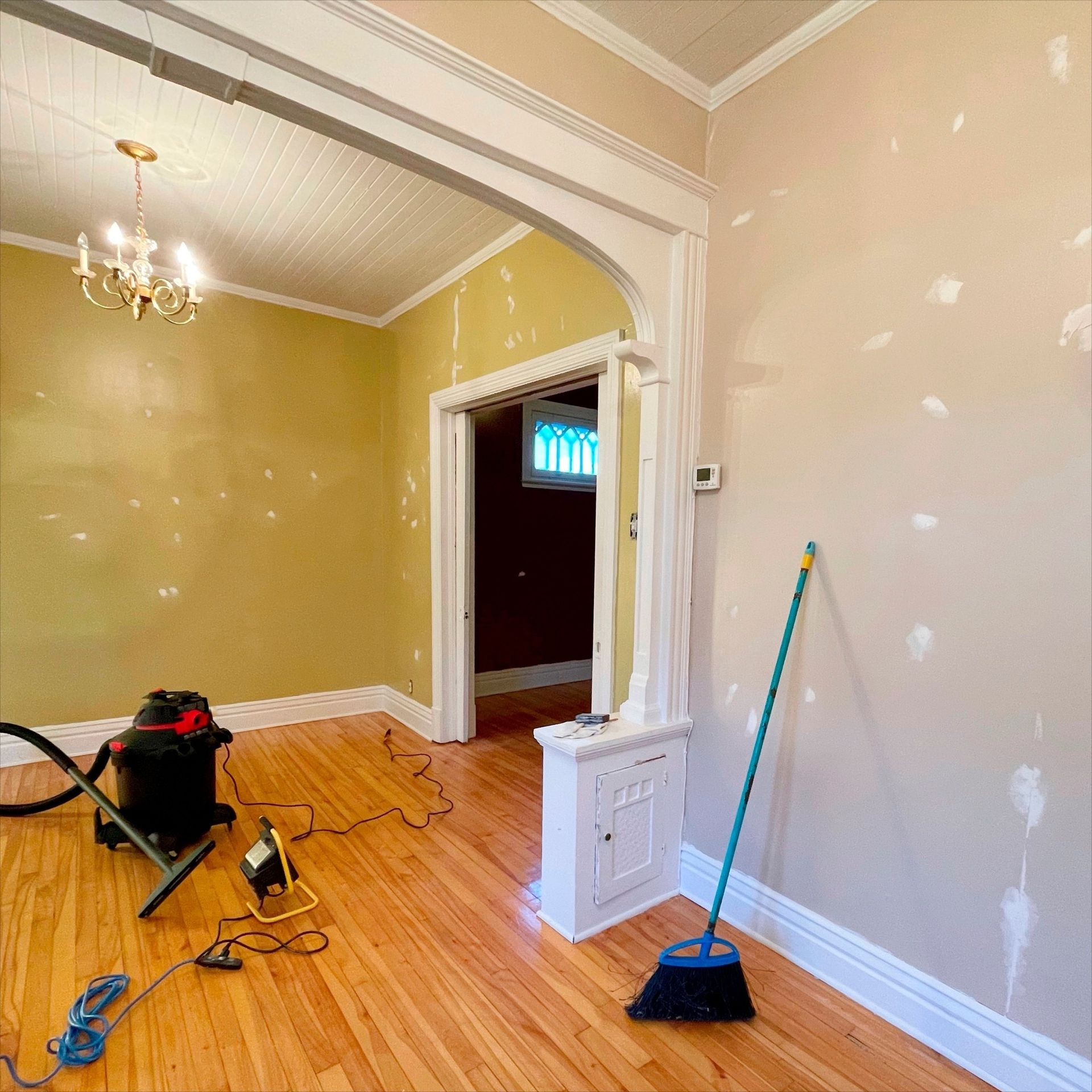 Room interior with wooden floors, partially painted walls, tools, and arched doorway.