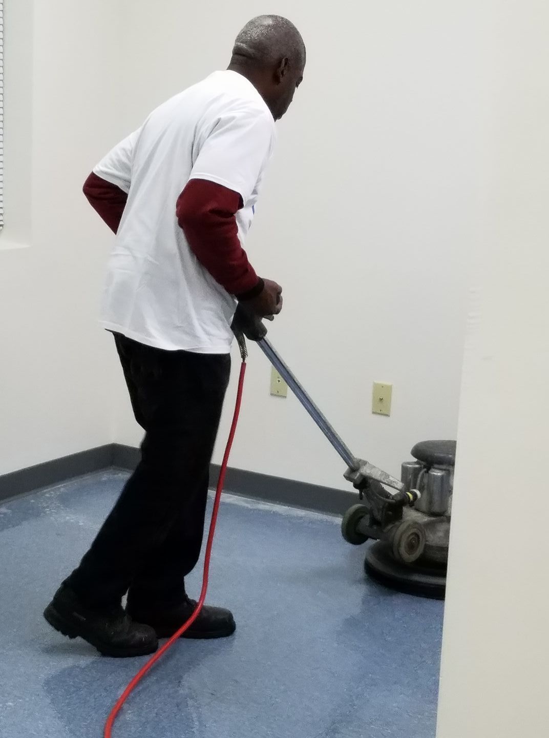 Man in white shirt and black pants polishing a blue floor in a room with white walls.