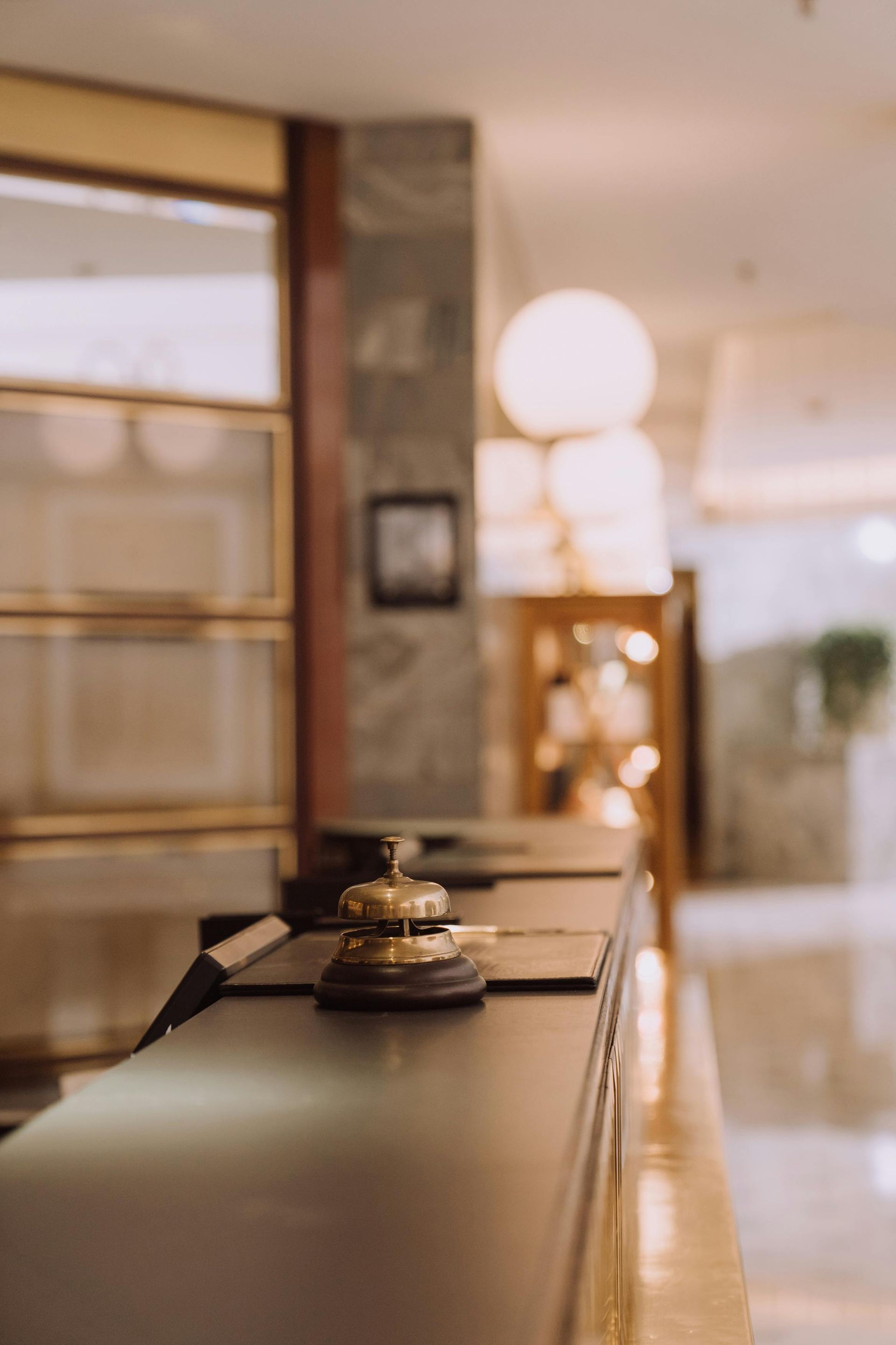 Hotel reception desk with bell in focus, soft lighting, and blurred background.