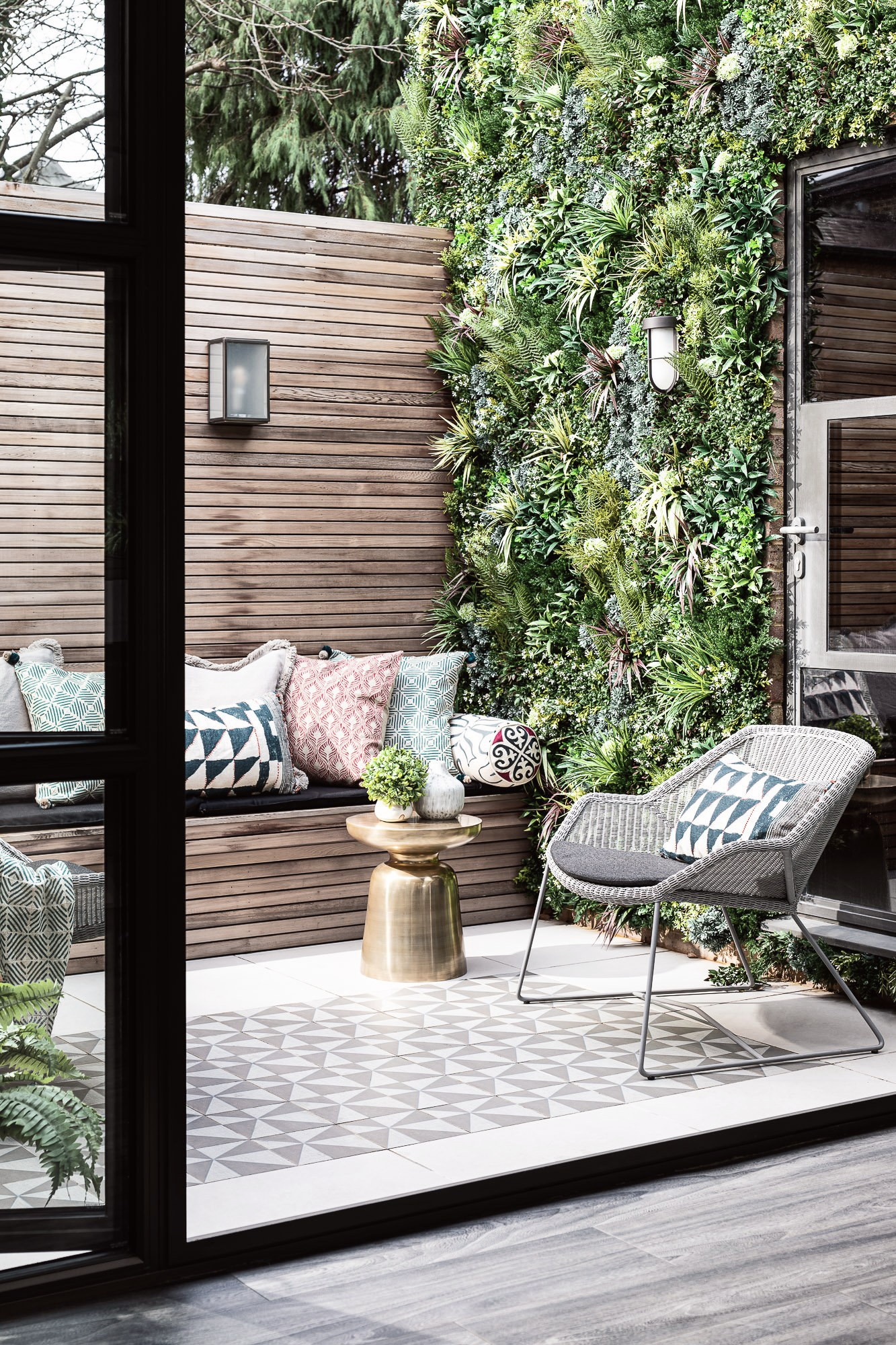 Leo Bancroft Modern patio with lounge chair, patterned rug, bench, and vertical garden wall behind glass doors