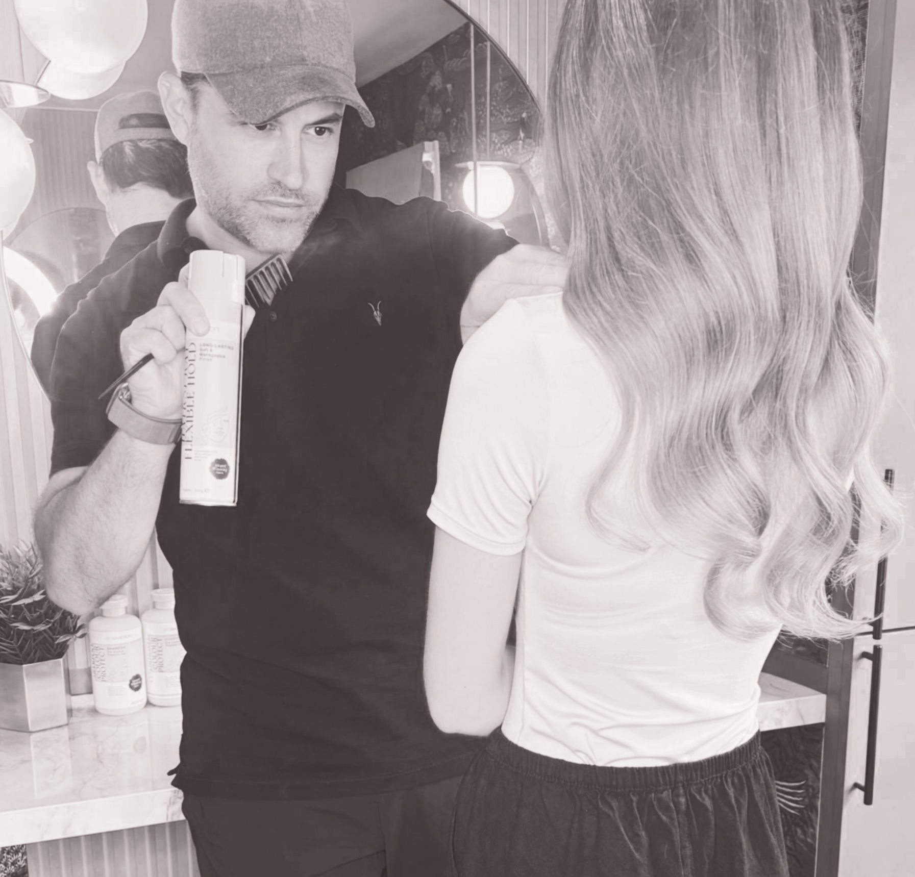 Leo Bancroft  curling a client’s hair at a salon mirror, with another woman reflected in the background