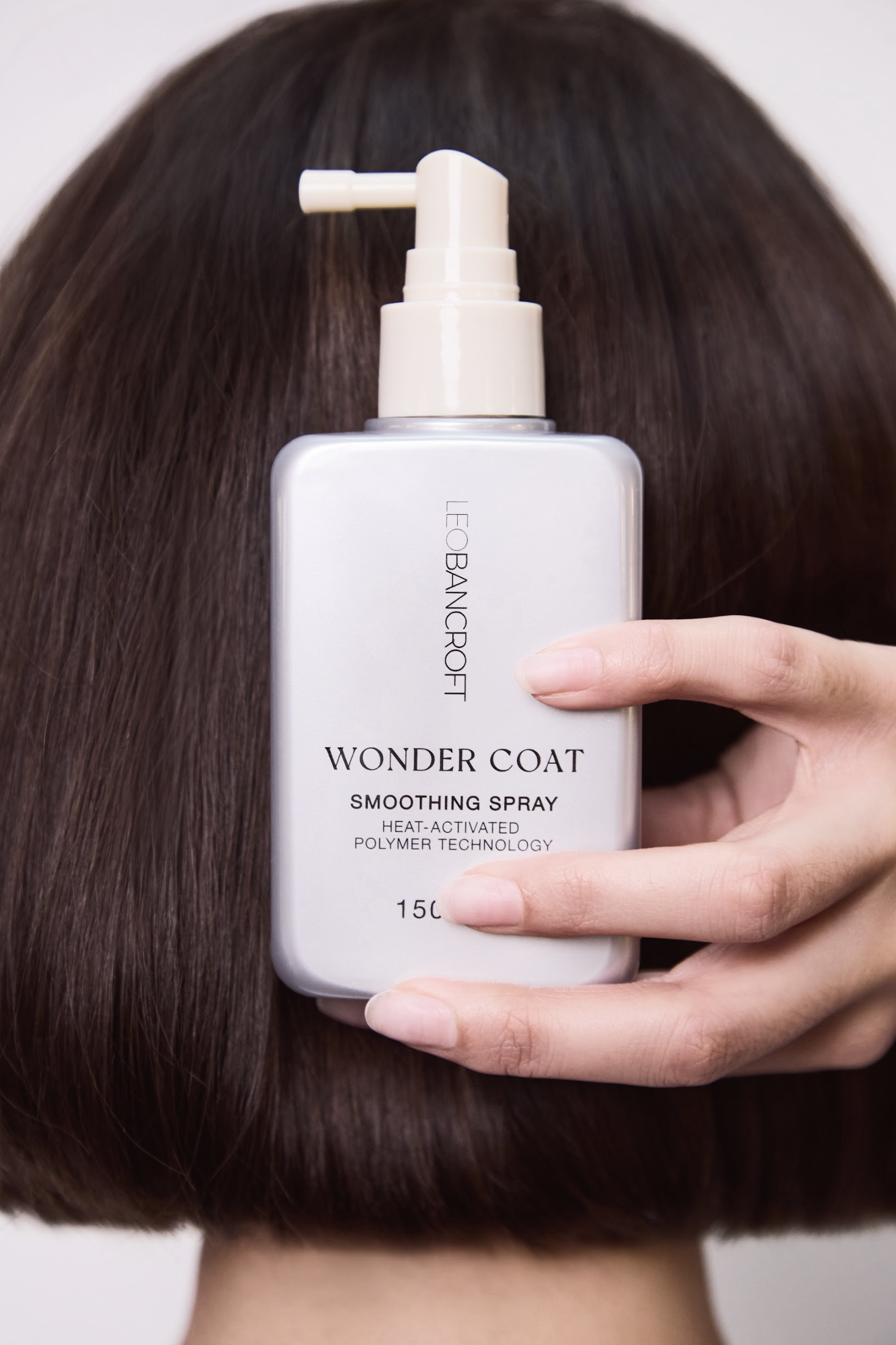 Hand holding a Leo Bancroft  hair product bottle in front of short dark brown hair