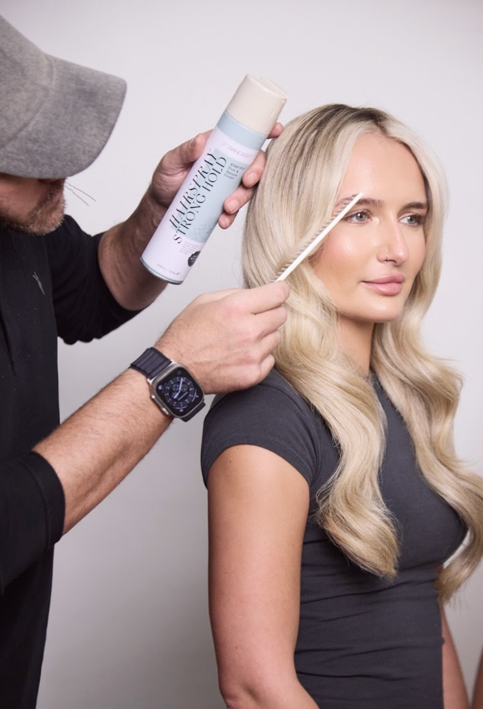 Leo Bancroft  curling a blonde woman’s hair with a curling iron and spray in a salon setting