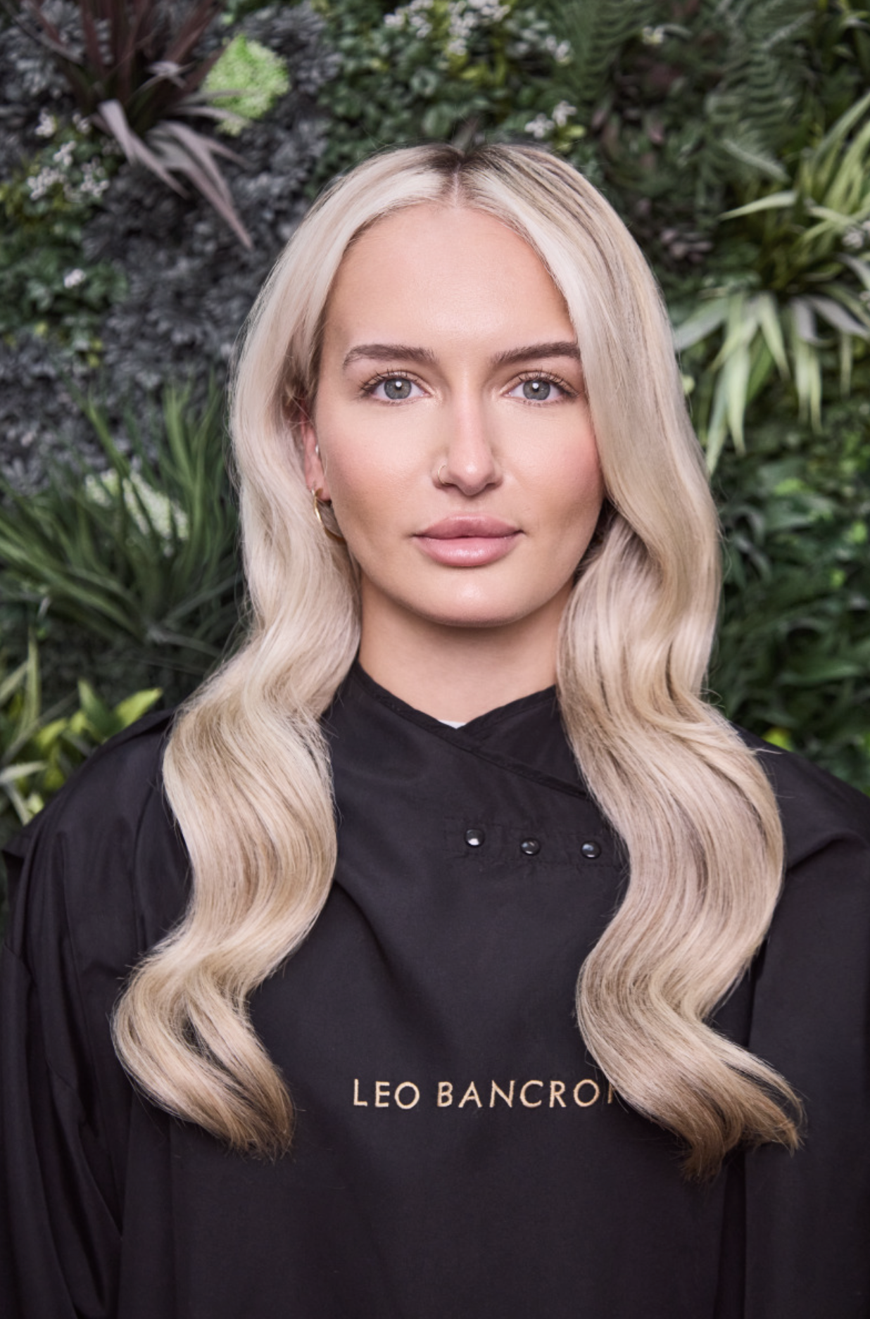 Blonde woman in a black hoodie posing against a leafy green backdrop