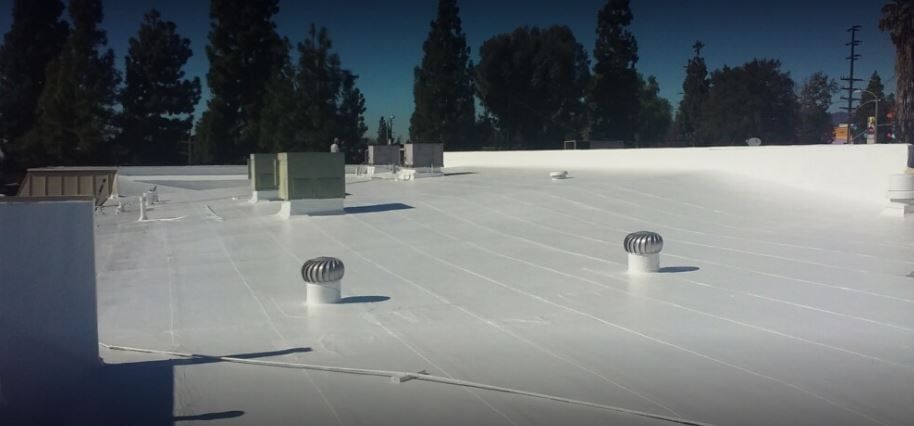 A man operates a nailer while installing shingles on a roof under clear blue skies