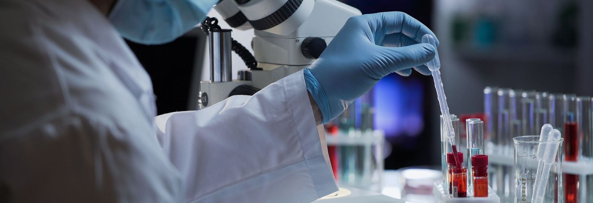 A scientist is looking through a microscope and pouring liquid into a test tube.
