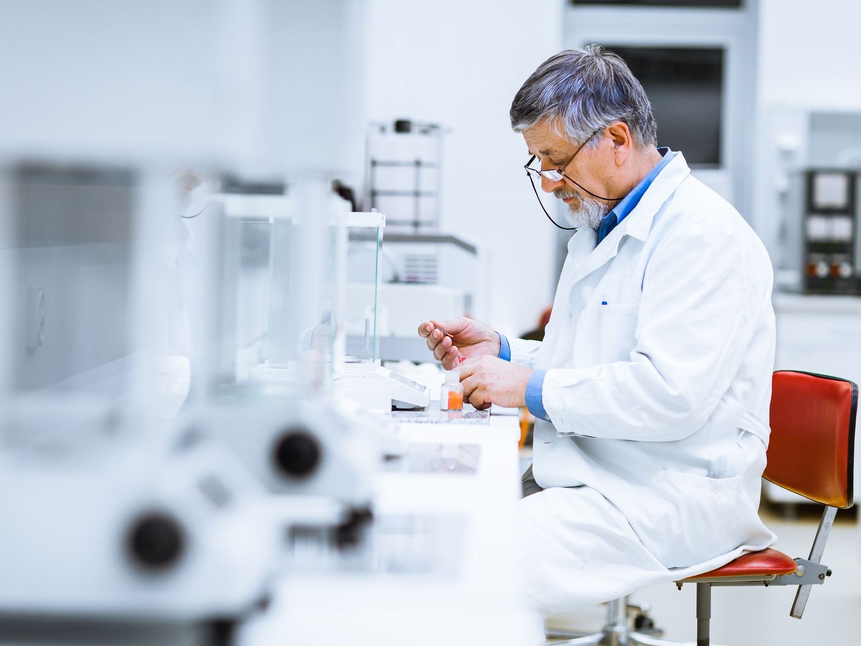 A man in a lab coat is sitting at a desk in a laboratory.