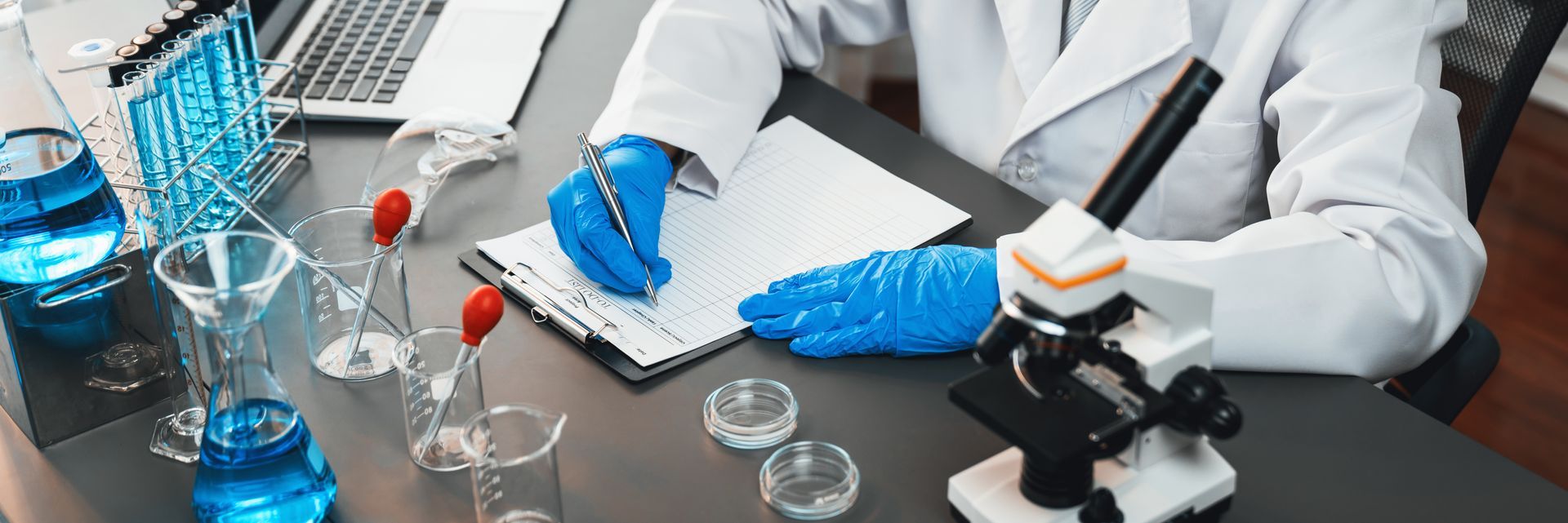 A scientist is sitting at a table with a microscope and writing in a notebook.