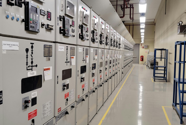 Electrical control panels lining a bright industrial hallway with a blue cart on the right.