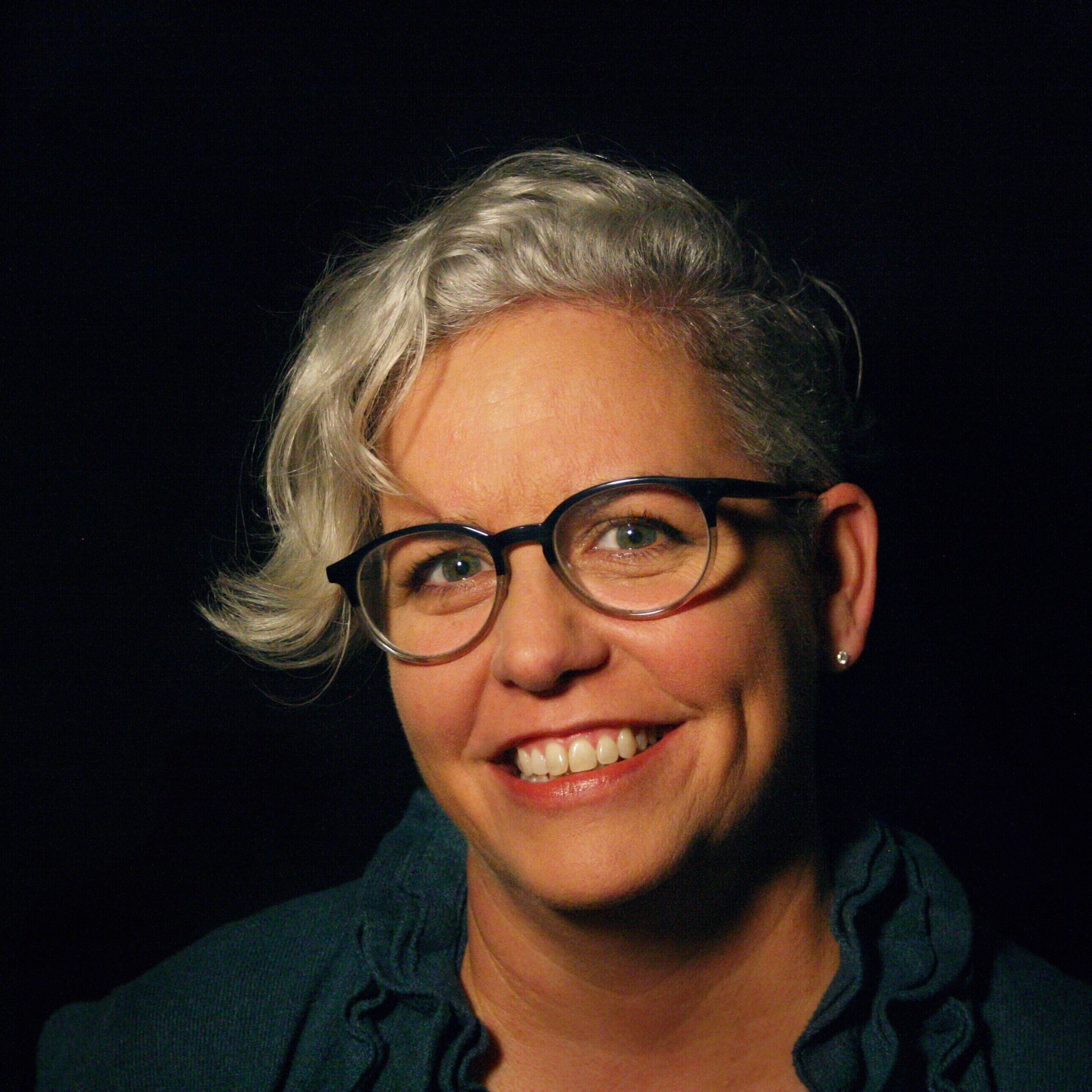 A woman wearing glasses and a blue shirt is smiling