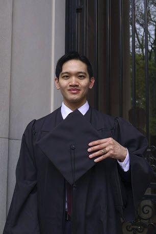 A man in a graduation cap and gown is standing in front of a building.