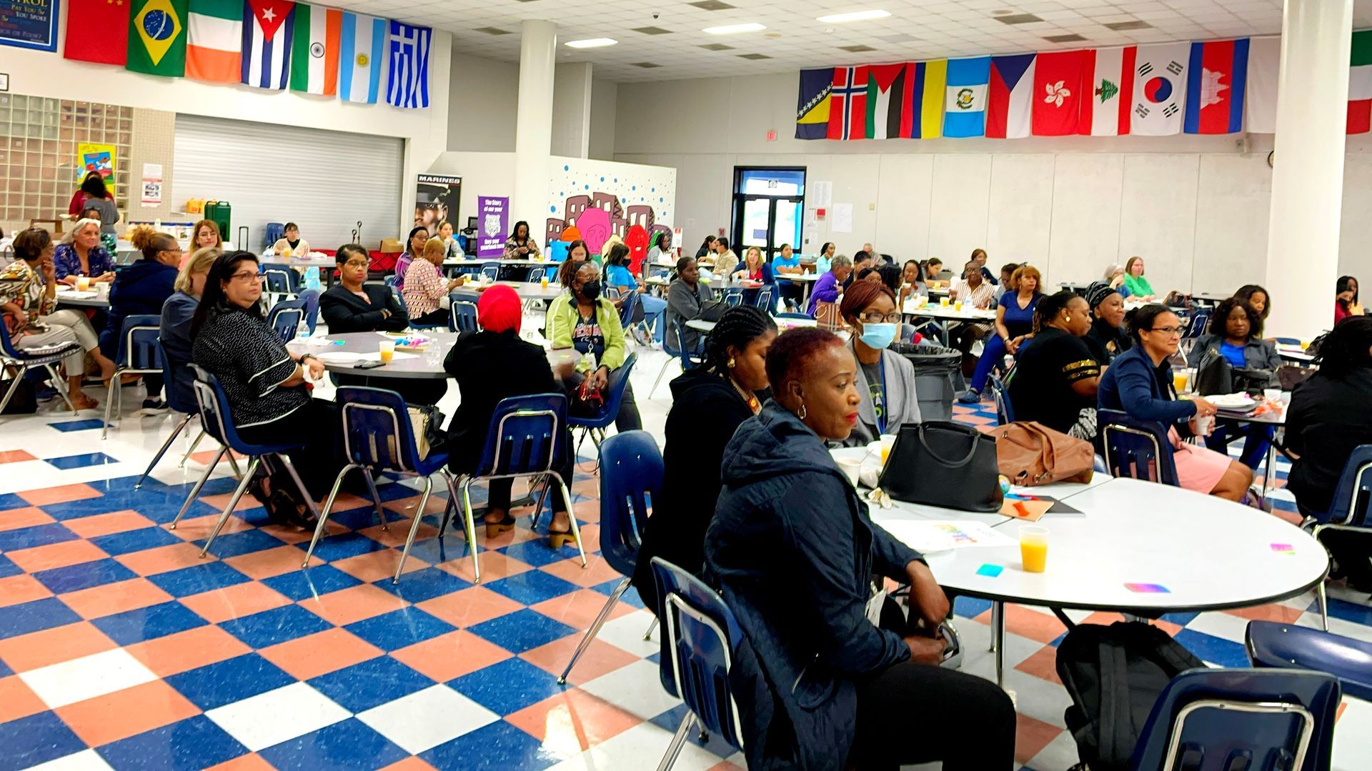 A large group of people are sitting at tables in a cafeteria.