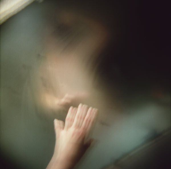 A blurry picture of a person 's hand touching a glass window.