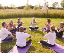 A group of people are sitting in a circle on yoga mats in a field.