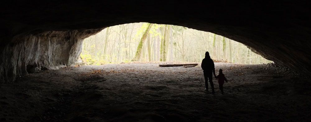 A man and a child are standing in a cave holding hands.