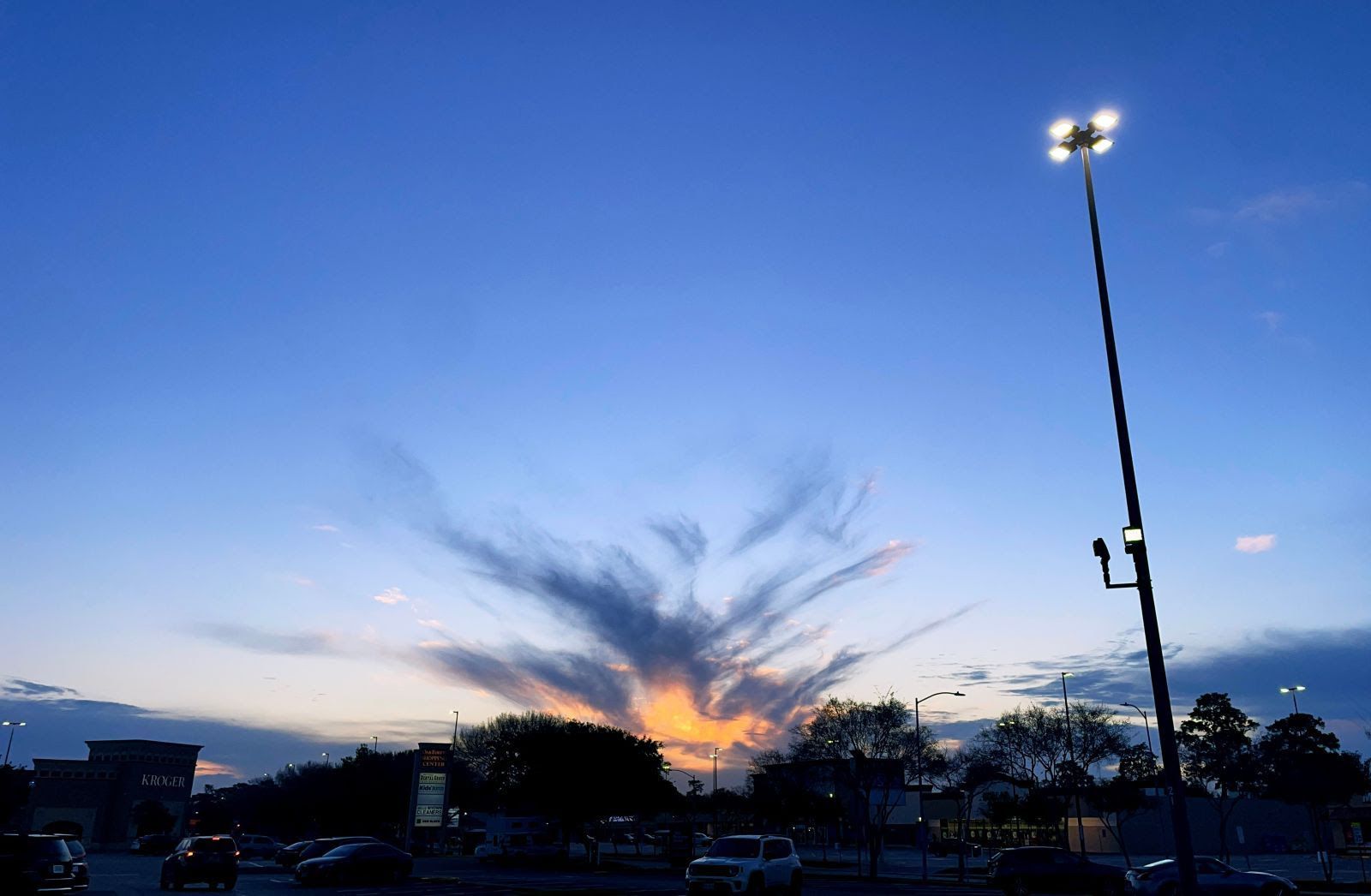 A street light in a parking lot with a sunset in the background