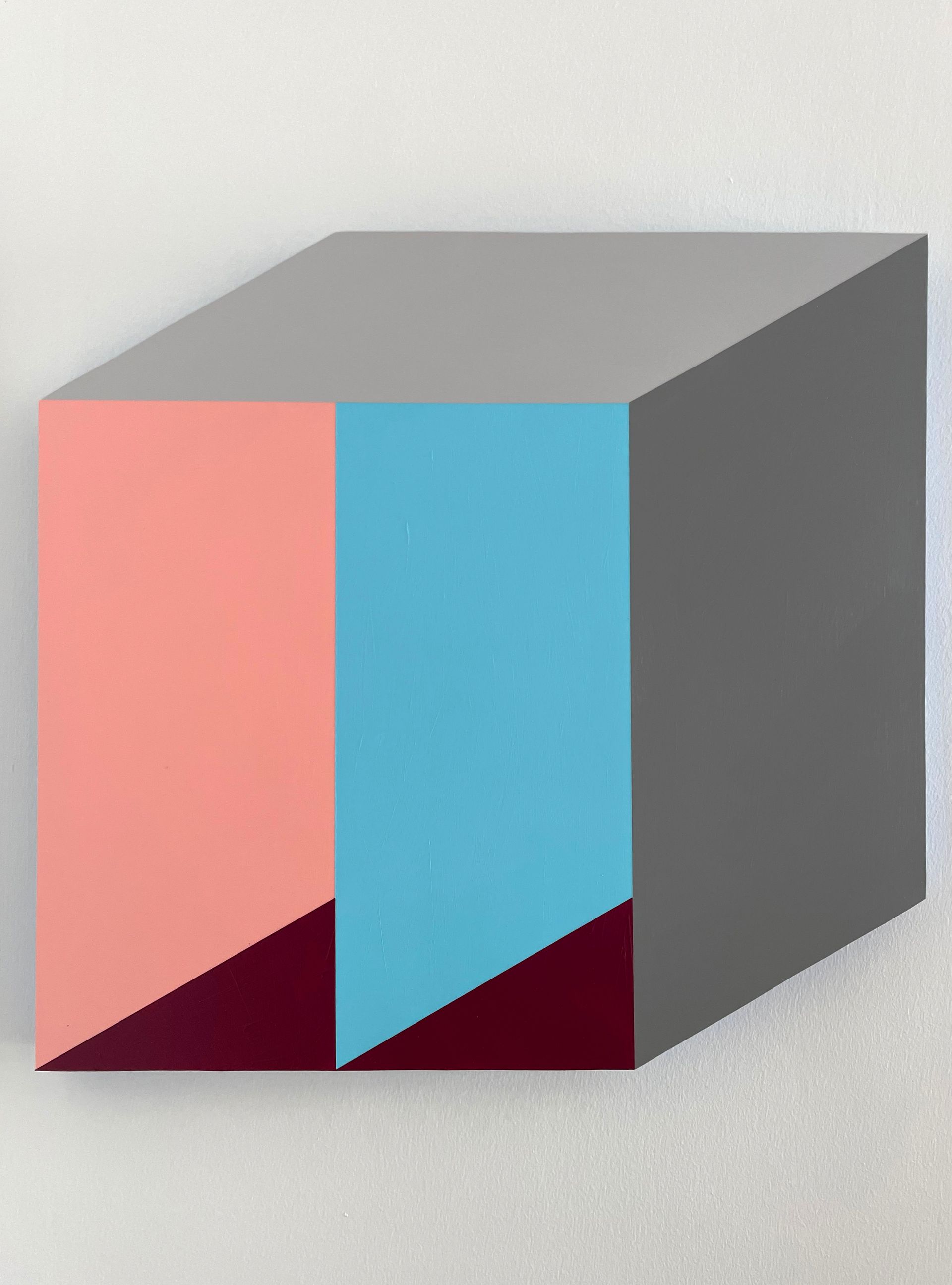 A gray cube with a pink, blue, and gray face. Dark red lines at the base.