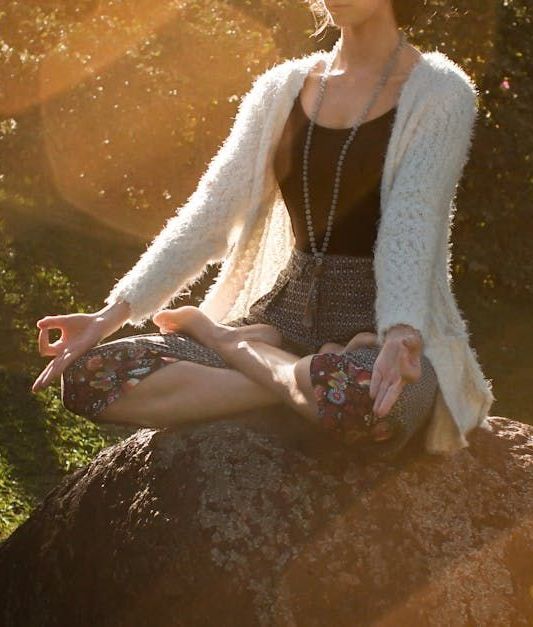 A woman is sitting in a lotus position on a rock