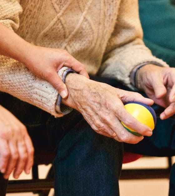 An elderly man is holding a yellow ball in his hand.