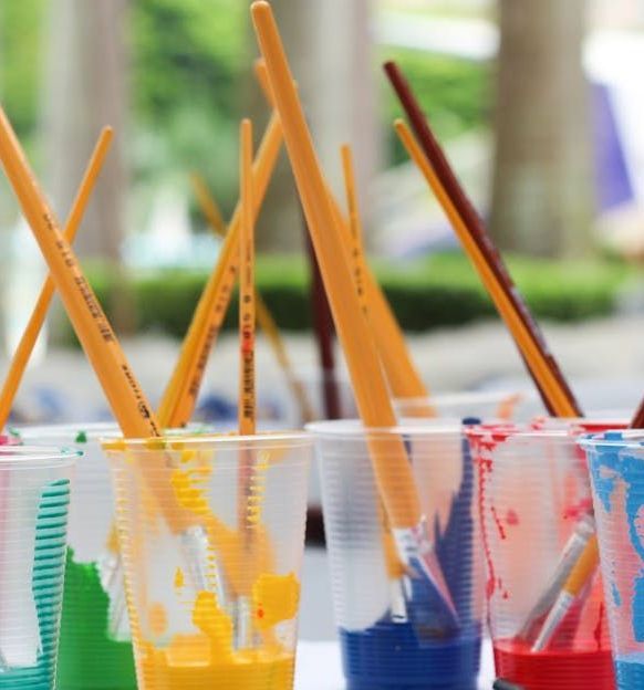 A row of plastic cups filled with different colors of paint and brushes