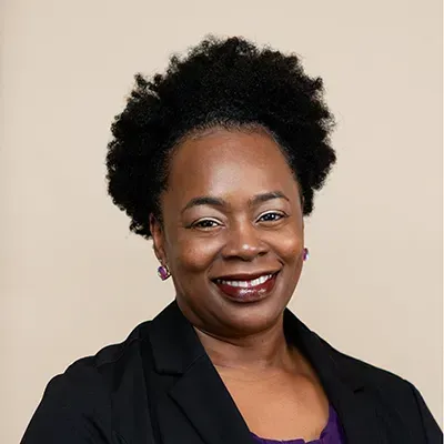 A woman in a black jacket and purple shirt is smiling for the camera.