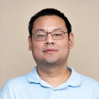 A man wearing glasses and a light blue shirt is looking at the camera.