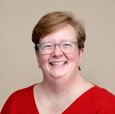 A woman wearing glasses and a red sweater is smiling for the camera.