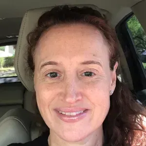 A woman is smiling while sitting in the back seat of a car.