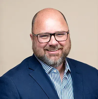 A man with a beard and glasses is wearing a blue suit and striped shirt.