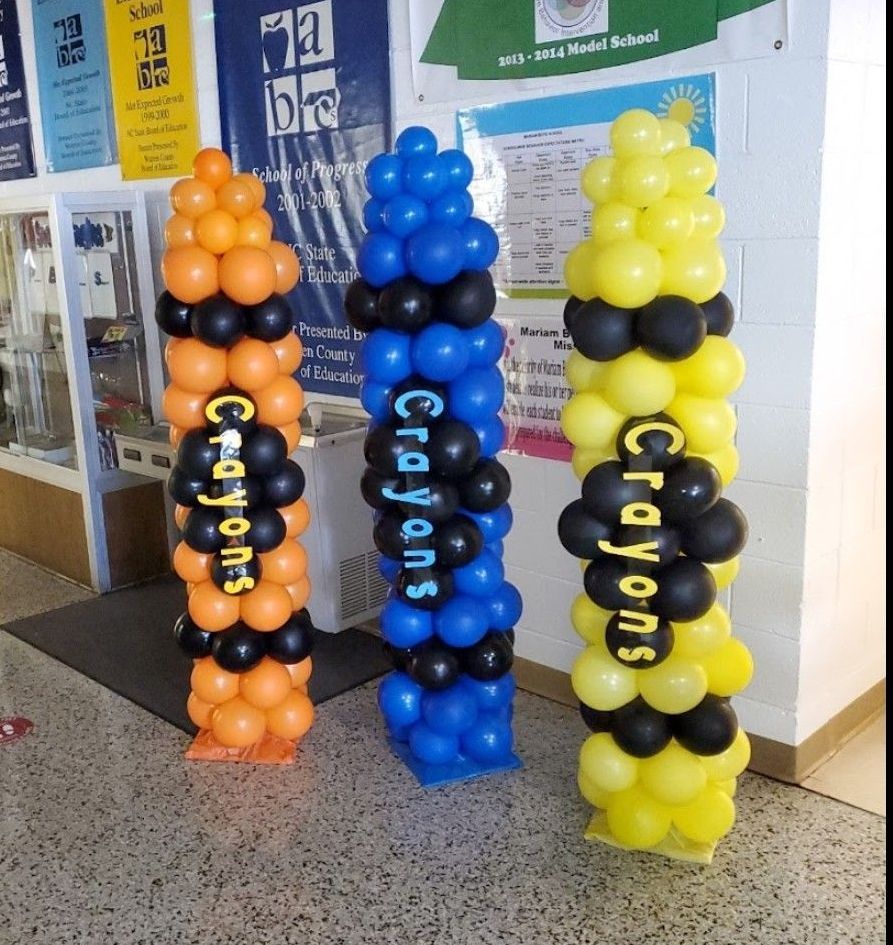 Three tall crayon-shaped balloon decorations in orange, blue, and yellow, with