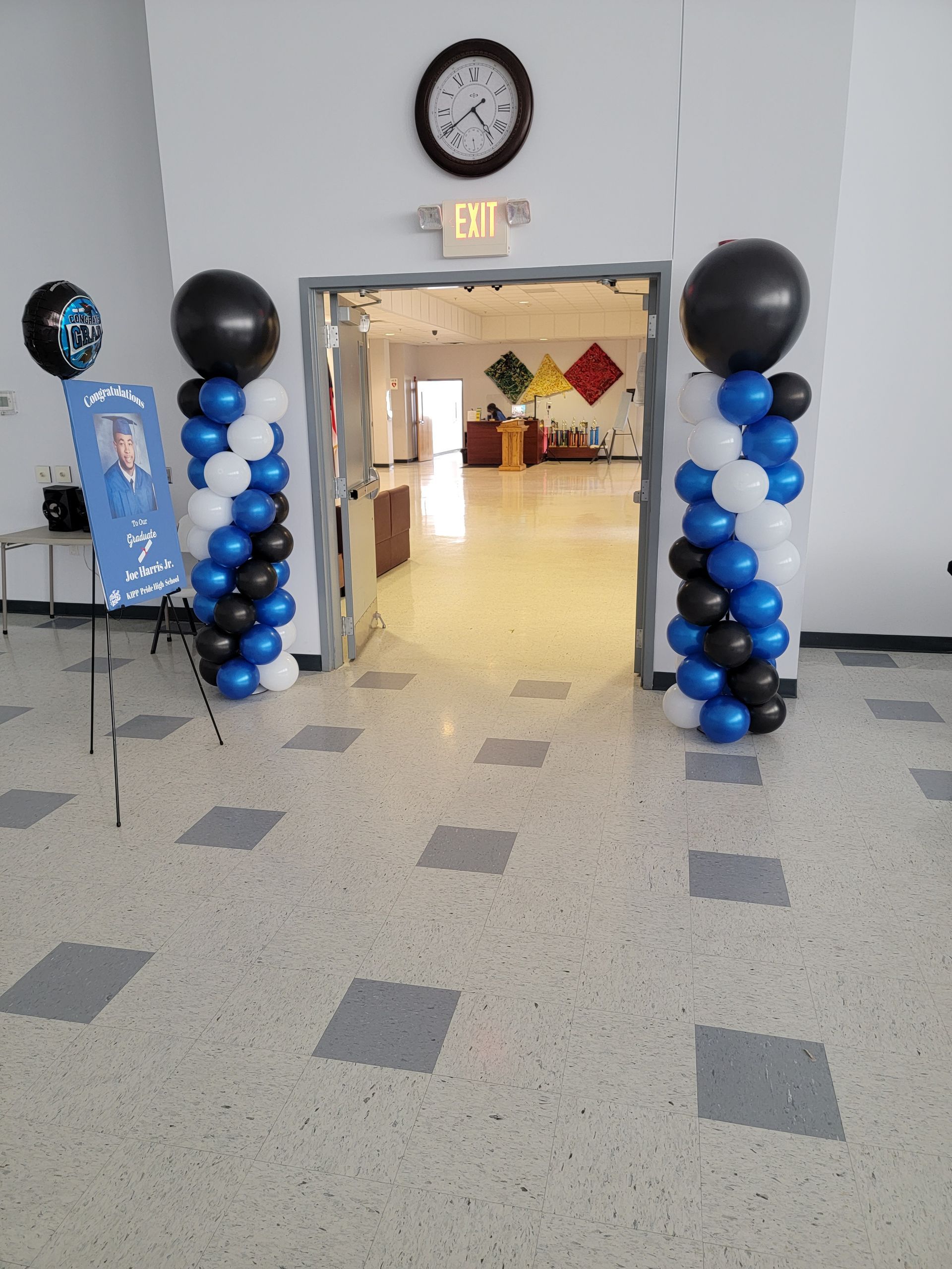 Entrance decorated with blue, black, and white balloon columns. A sign stands to the left.