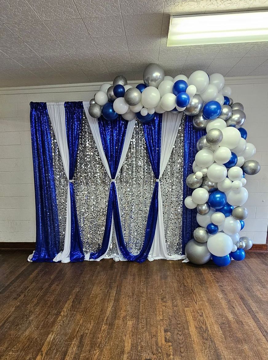 Blue and silver backdrop with balloon arch, set on a wooden floor.