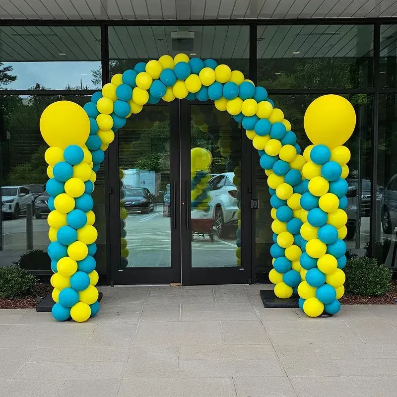 Yellow and teal balloon arch over glass doors, flanked by columns of balloons.